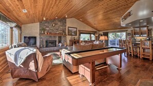 Amplio salón con mesa de billar, asientos cómodos, chimenea de piedra y zona de cocina con taburetes de madera.