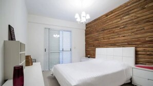 Un dormitorio con una pared de acento de madera, una cama blanca, una mesita de noche y una lámpara de noche.