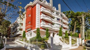 Un edificio de varios pisos con balcones, una entrada protegida por una reja y un área ajardinada con árboles.
