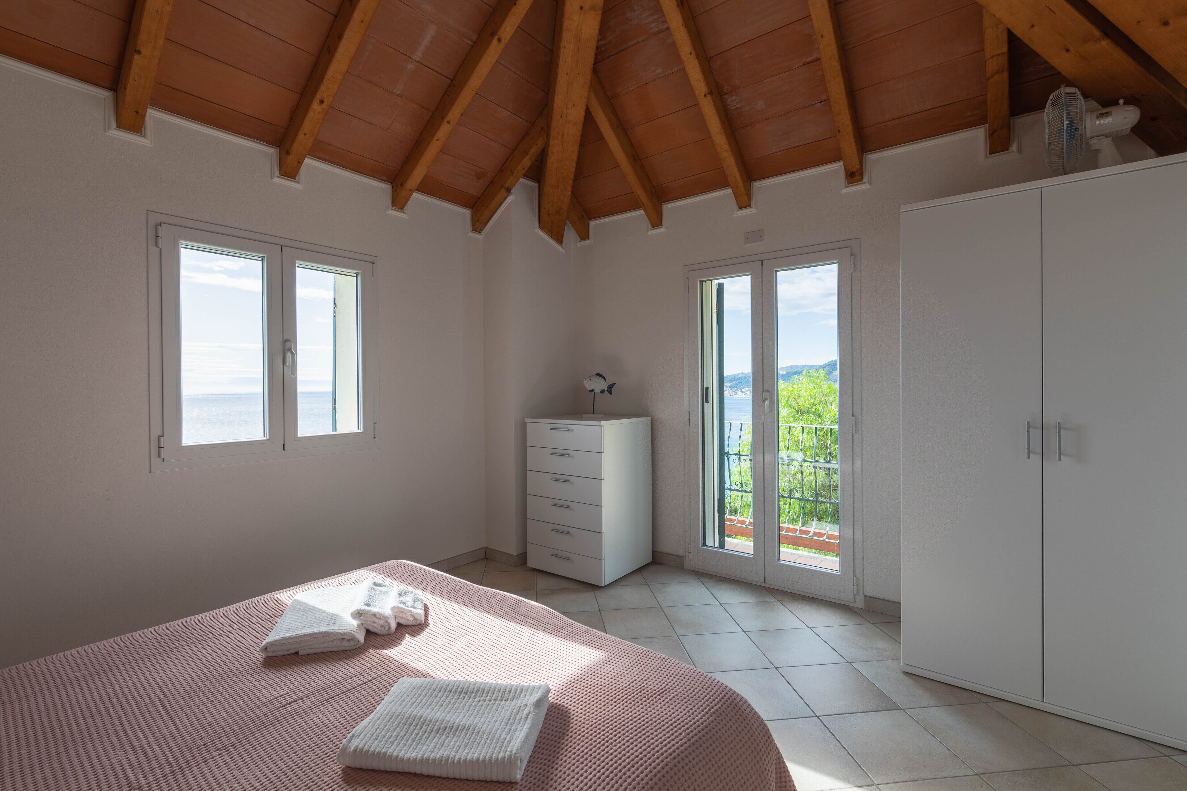 Ein Schlafzimmer mit Bett, Kommode, Kleiderschrank und einer Glasschiebetür, die auf einen Balkon führt.