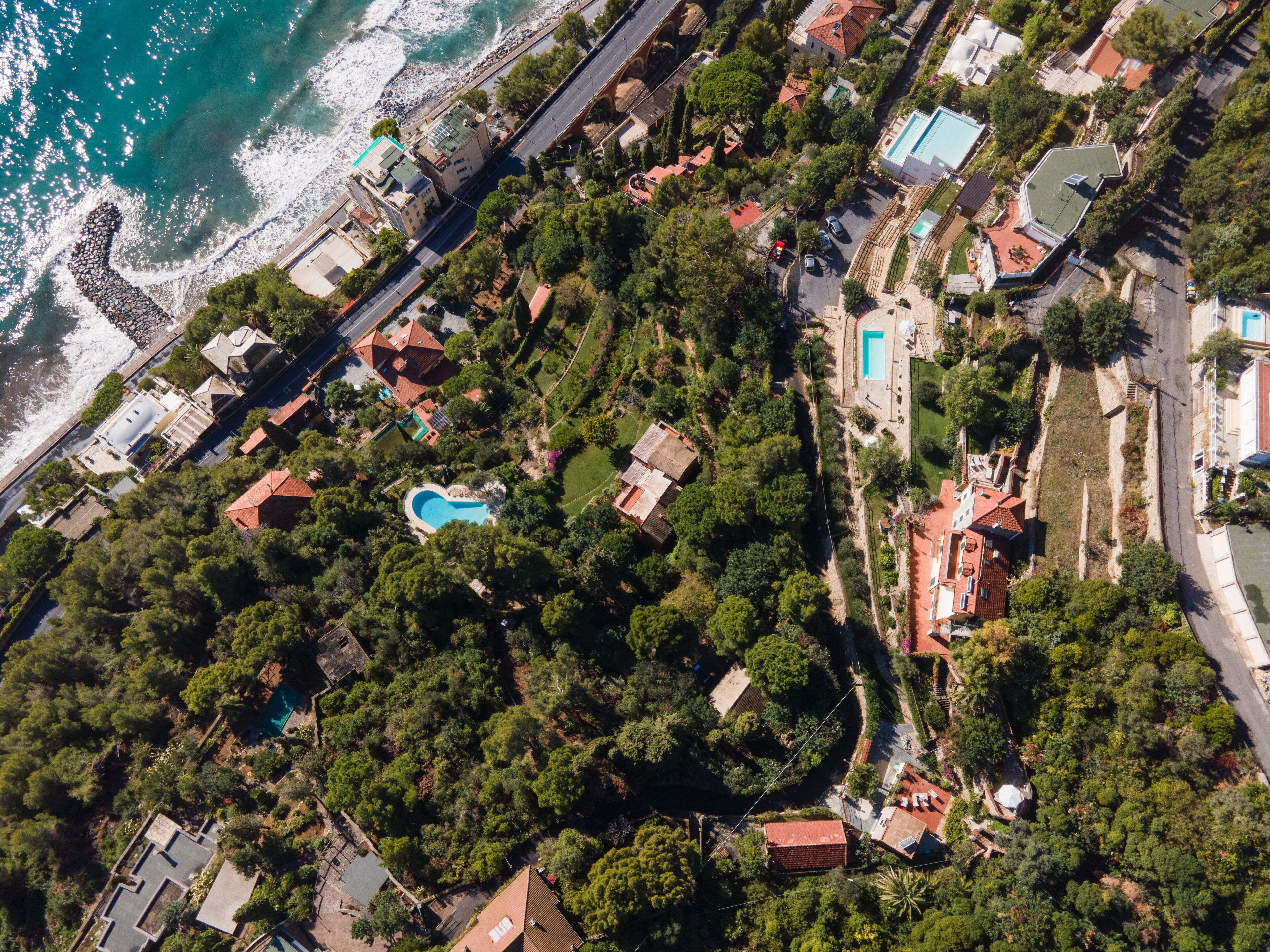 An aerial view of a coastal residential area with houses, a swimming pool, and a beach.