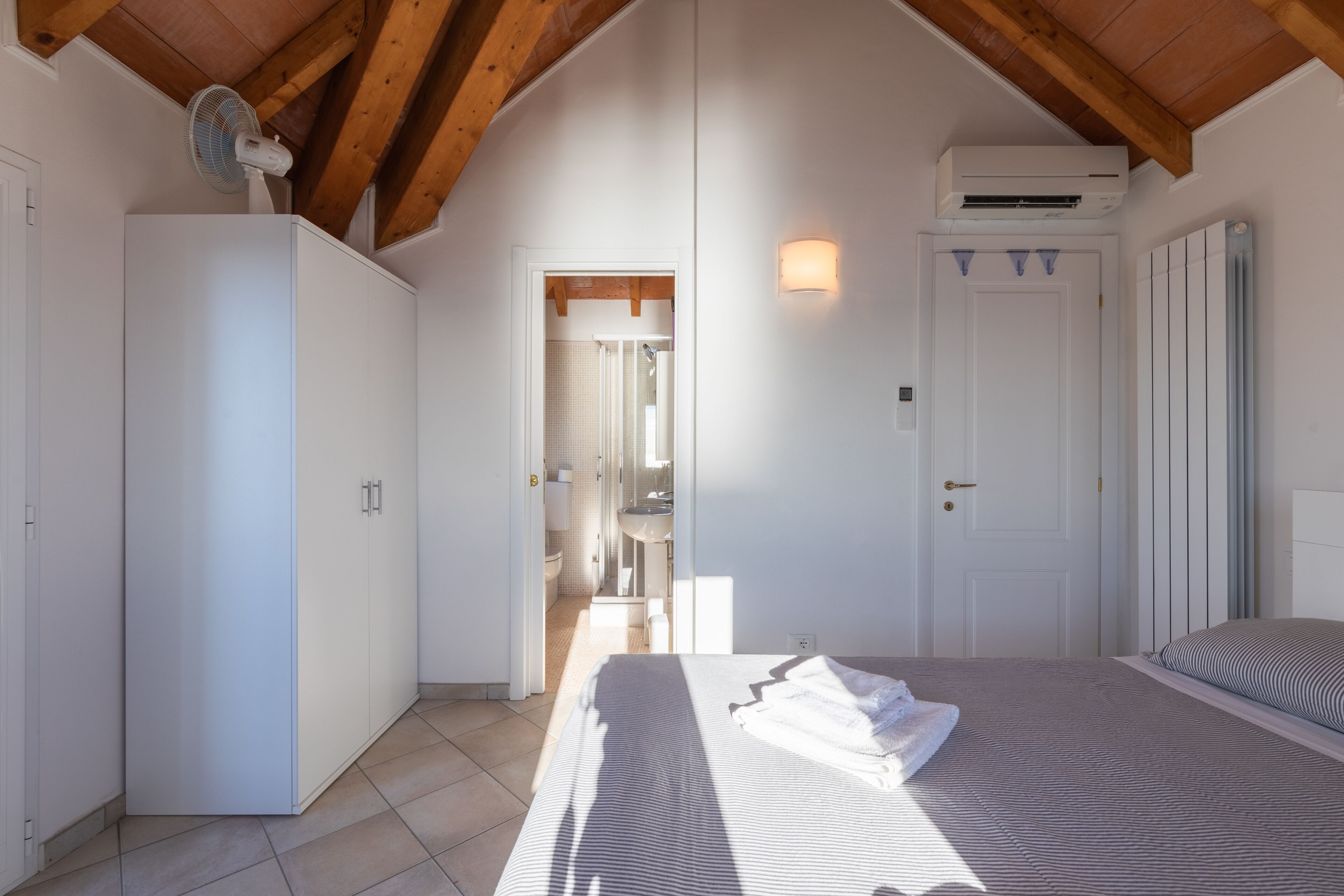 A bedroom with a bed, a wardrobe, and a bathroom visible through an open door.