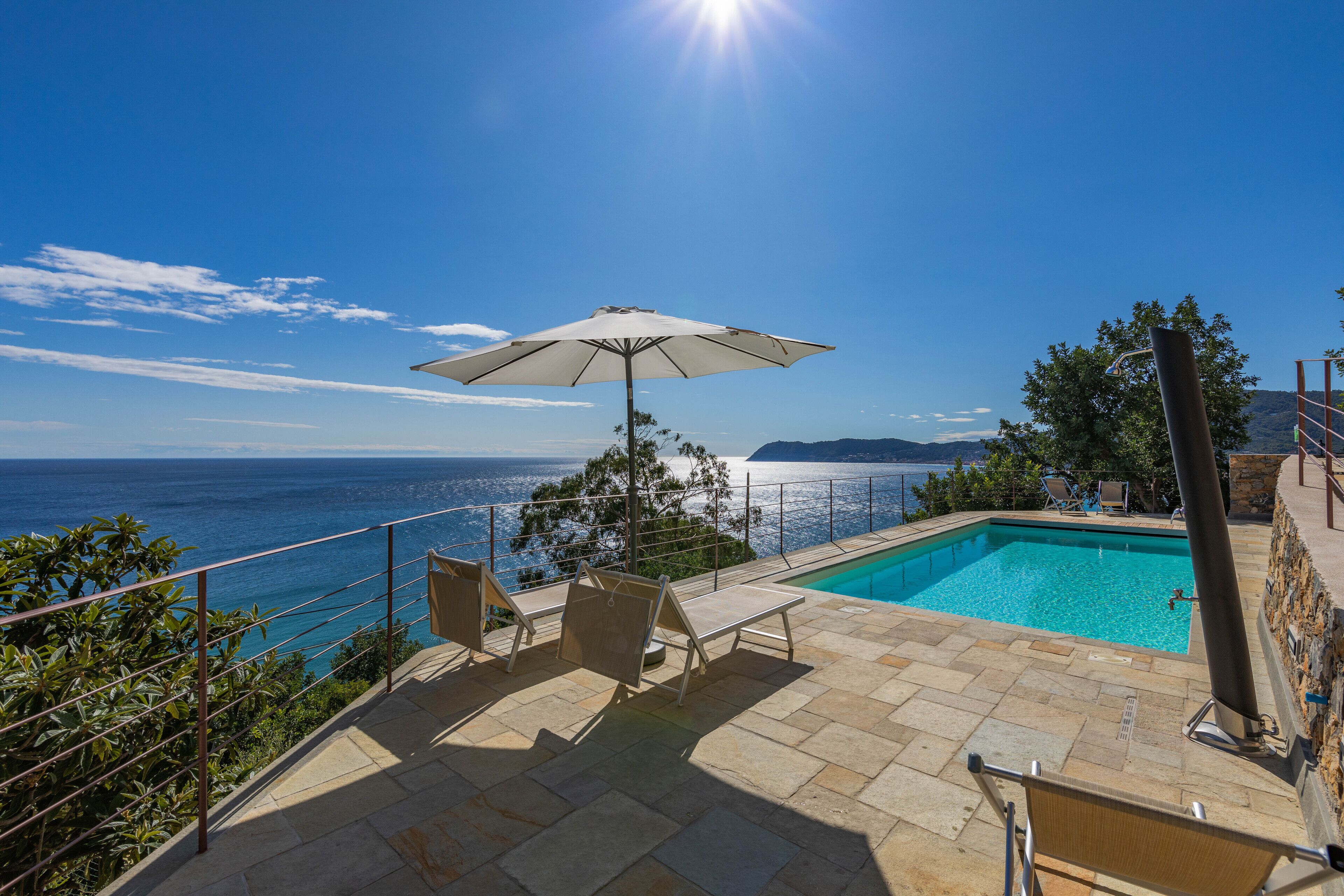 Zona de piscina con vistas al mar, una silla de descanso y una sombrilla.
