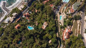 Vista aérea de una zona residencial costera con una llamativa piscina en forma de corazón, rodeada de exuberante vegetación y casas con tejados rojos.