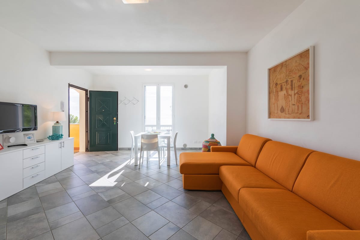 A modern living room with a sectional sofa, a flat-screen TV, a dining table with chairs, and a green door leading to another room.