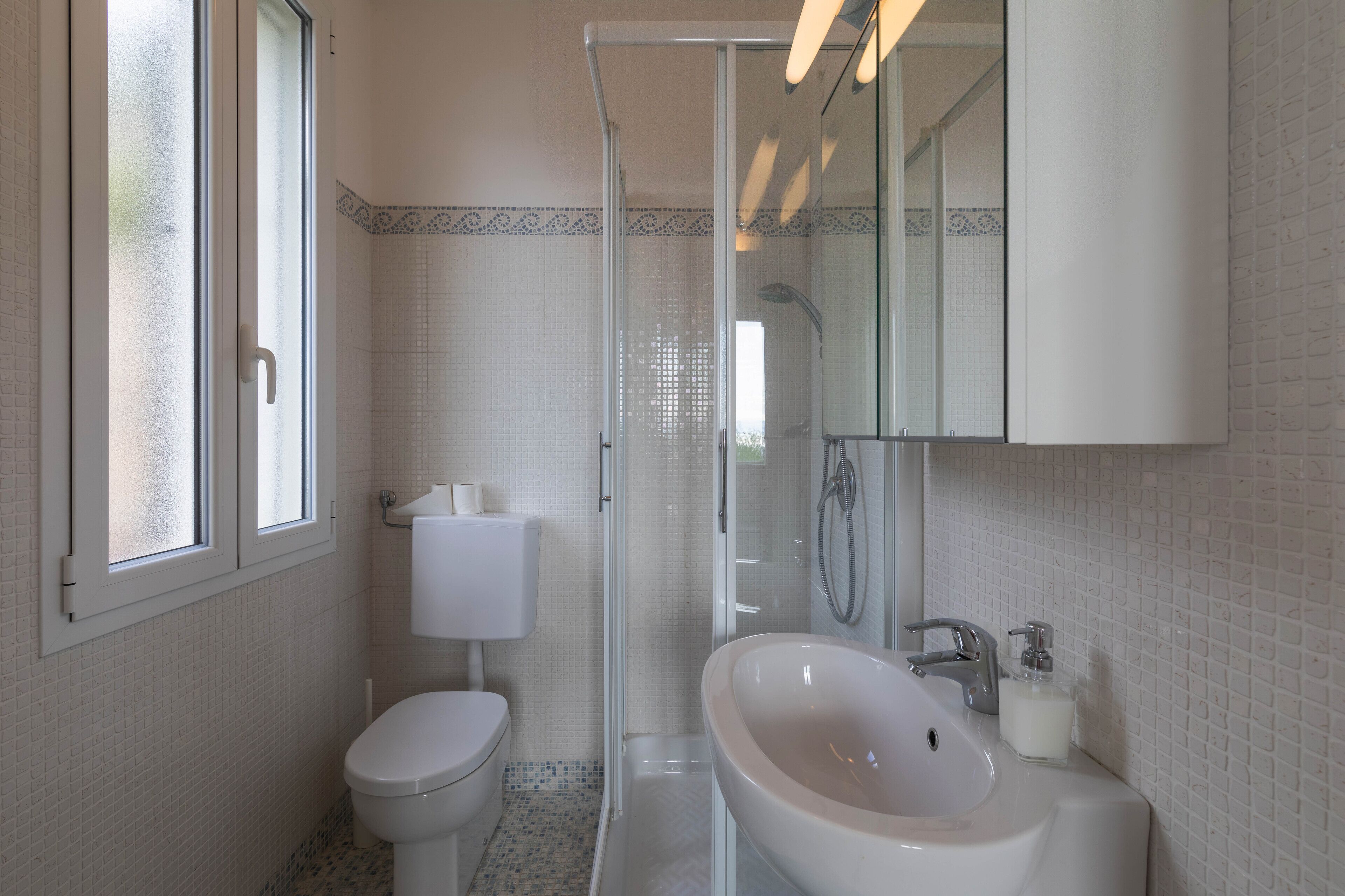 A bathroom with a toilet, a sink, a shower, and a mirror.