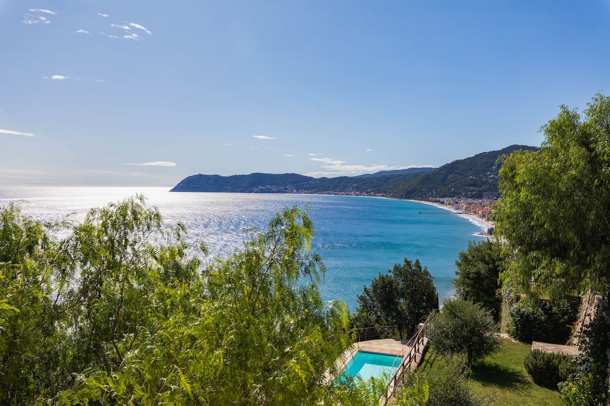A coastal view with a clear sky, a swimming pool, and lush greenery.