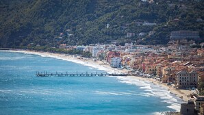 Un paisaje urbano costero con una playa, edificios y un muelle que se adentra en el mar.