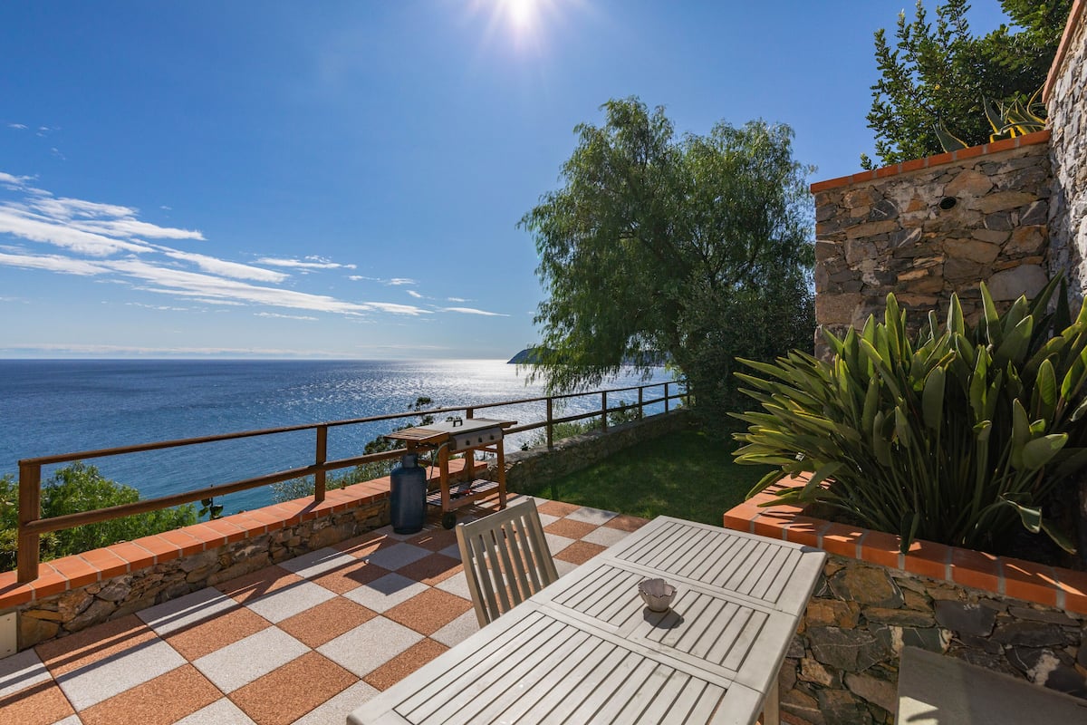 A patio with a checkered floor, a table, chairs, and a view of the sea.