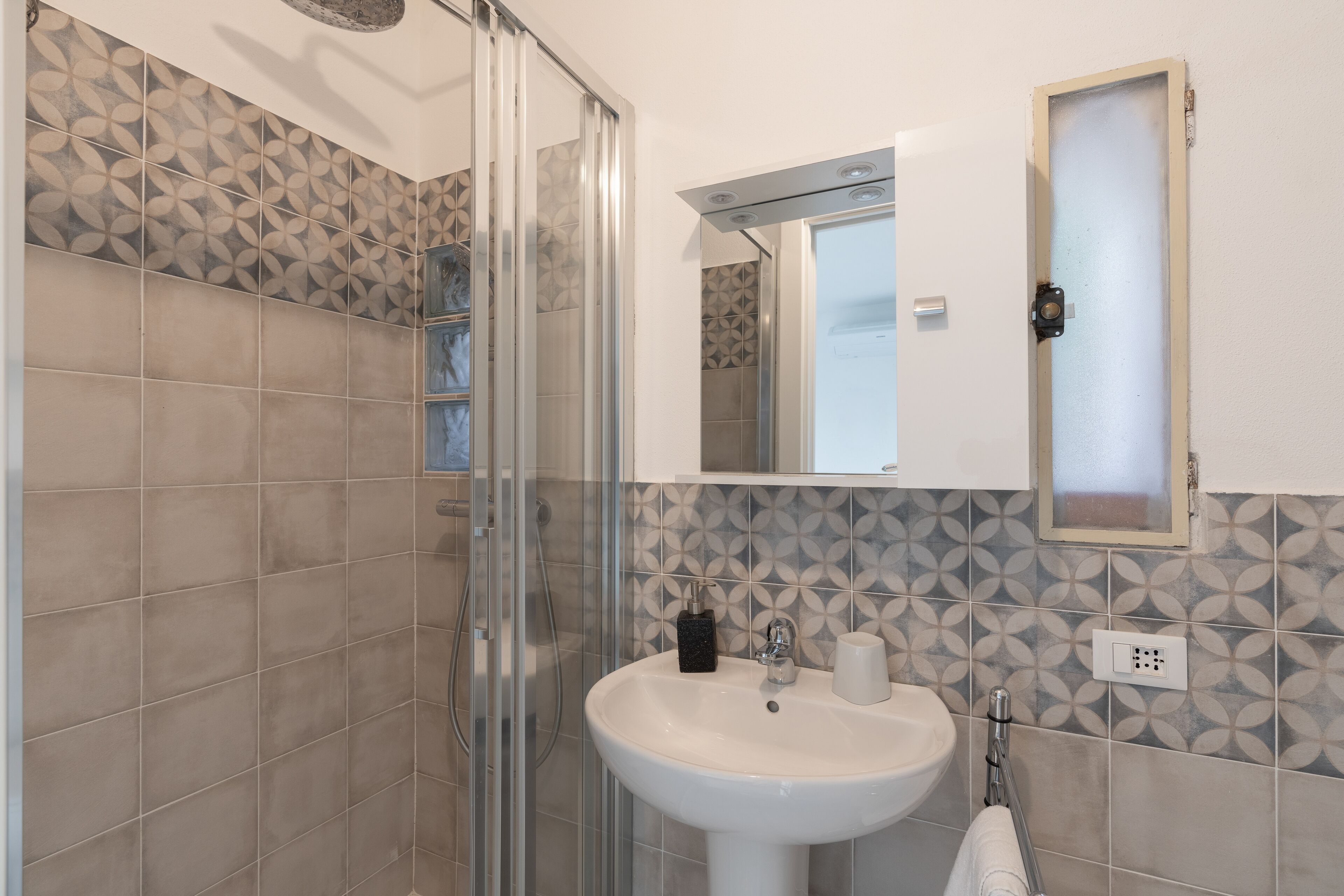 Une salle de bain avec une douche à parois de verre, un lavabo blanc et un miroir au-dessus du lavabo.