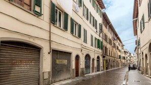 A narrow cobblestone street lined with buildings featuring arched doorways and green shutters. - Cennano Suite - enter apartment (Montevarchi)
