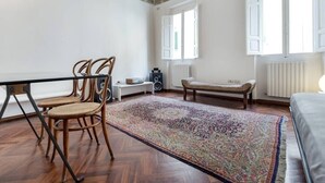 A room with a wooden floor, a patterned rug, a bench, a table with chairs, and a radiator. - Cennano Suite - enter apartment (Montevarchi)