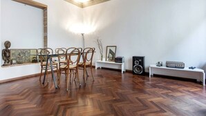 A room with a wooden herringbone floor, a dining table with chairs, a white bench, a speaker, and a framed picture on the wall. - Cennano Suite - enter apartment (Montevarchi)