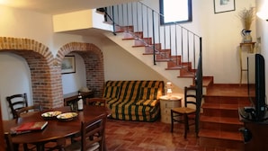 Un área de comedor con un arco de ladrillo, un sofá a rayas y una escalera con barandilla.
