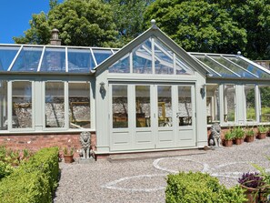 A conservatory with a brick exterior, large glass windows, and a decorative lion statue in front. - 1 bedroom accommodation in Pitscandly, near Forfar (Pitscandly, near Forfar)