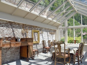 A conservatory with a brick wall, wooden furniture, and a table set for dining.