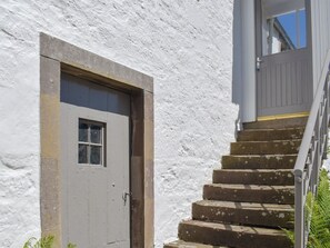 A white building with a grey door and a set of stone steps leading to a window.