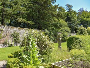 A garden with a stone wall, various plants, and a wooden structure. - 1 bedroom accommodation in Pitscandly, near Forfar (Pitscandly, near Forfar)