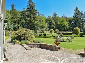 A well-maintained garden with a stone pathway, a seating area with chairs and a table, and a decorative urn.