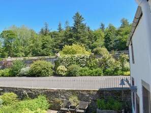 A stone wall with a bench and a bicycle, surrounded by lush greenery and flowering plants.