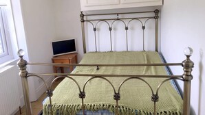 A metal-framed bed with a green blanket, a white cabinet above, and a small wooden table with a TV in a room with white walls. - Aparthotel Crystal Palace (London)