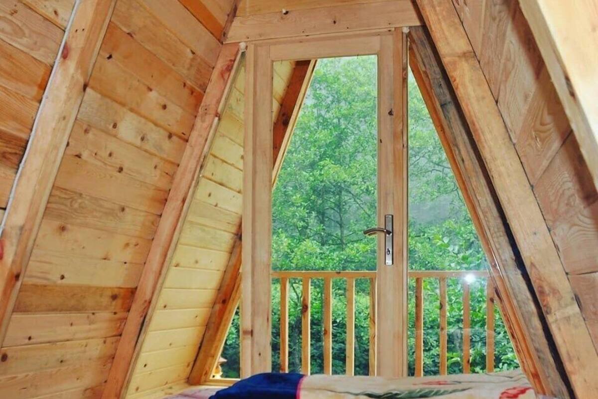Une chambre mansardée en bois, avec un lit, une fenêtre et une vue sur la verdure environnante.