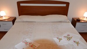 Ein ordentlich bezogenes Bett mit einem hölzernen Kopfteil, zwei Nachttischen mit Lampen und einer floralen Tagesdecke.