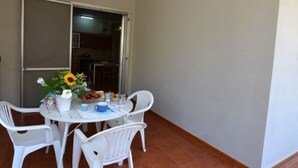 Ein kleiner Essbereich mit einem runden Tisch, vier weißen Stühlen, einer Vase mit Blumen und Blick zur Küche durch eine offene Tür.