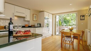 Una cocina moderna con armarios blancos, una zona de comedor con mobiliario de madera y vistas a zonas verdes a través de la puerta.