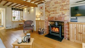 Una sala de estar acogedora con vigas de madera a la vista, una chimenea de ladrillo, un televisor y un sillón cómodo.