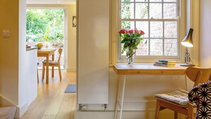 Una habitación con un escritorio de madera, una silla, un ventanal con vista a la vegetación y una lámpara sobre el escritorio.