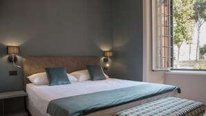Un dormitorio con cama, lámparas de noche, ventana y un banco.