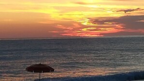 A beach scene with a sunset, a beach umbrella, and lounge chairs. - Apartment with garden overlooking the sea (Torremezzo di Falconara)