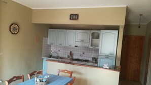 A compact kitchen with white cabinets, a tiled backsplash, and a dining area with a blue tablecloth. - Apartment with garden overlooking the sea (Torremezzo di Falconara)