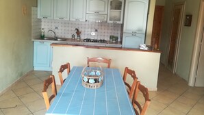 A kitchen with light blue cabinets, a tiled backsplash, and a dining area with a blue tablecloth and wooden chairs. - Apartment with garden overlooking the sea (Torremezzo di Falconara)