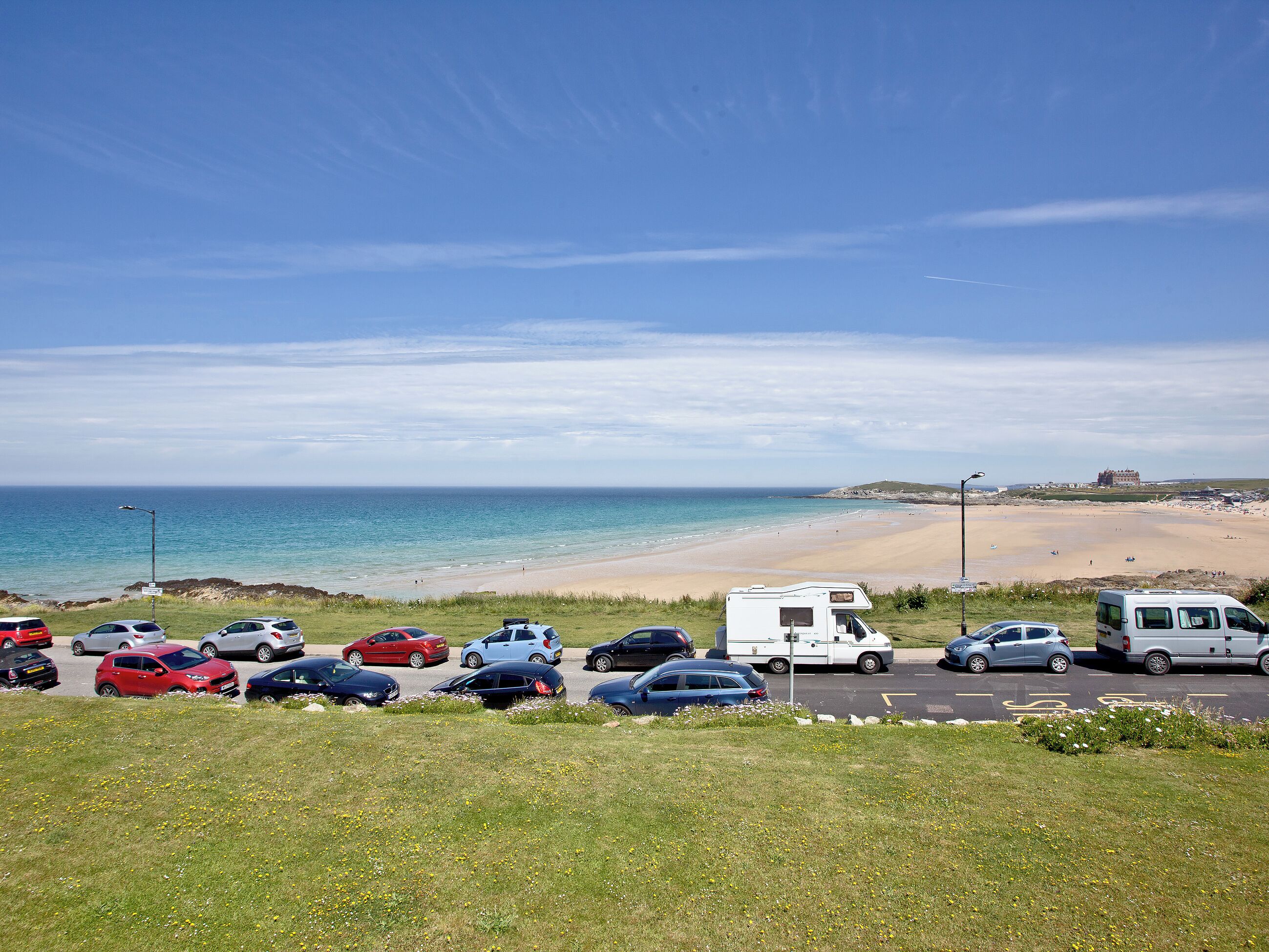 Ein Parkplatz mit Autos und einem Wohnwagen, mit Blick auf einen Strand und einen klaren Himmel.