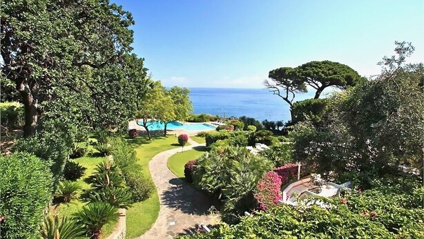 Un exuberante jardín con un sendero sinuoso, una piscina y vistas al océano.
