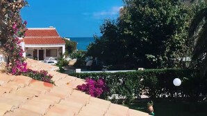A coastal building with a red-tiled roof, surrounded by lush greenery and vibrant pink bougainvillea flowers. - Denia beach, ideal for families (Dénia)