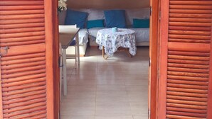 A room with a wooden door, a sofa with blue cushions, a small table with a white tablecloth, and two framed pictures on the wall. - Denia beach, ideal for families (Dénia)