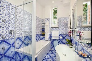 A bathroom with a white bathtub, a glass-enclosed shower, and a sink with a blue patterned backsplash. - IL GIARDINO DI POSITANO (Positano)