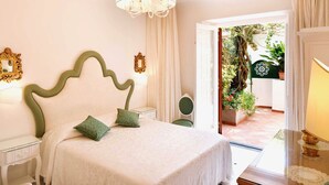 Una camera da letto con un letto, comodini, un lampadario e vista su un giardino attraverso una porta aperta.