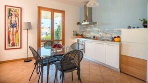 Uma cozinha moderna com armários brancos, painel de azulejos e um espaço de jantar com mesa de vidro e cadeiras de metal.