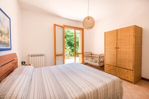 Ein Schlafzimmer mit Bett, Kleiderschrank, Heizkörper, einer zur Außenseite führenden Tür und einer Pendelleuchte.
