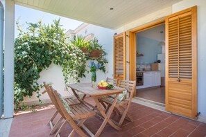 Eine Terrasse im Freien mit einem Holztisch und Stühlen, einem Korb voller Zitronen und Blick in die Küche durch offene Holztüren.