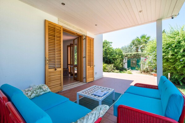 A covered patio with blue and red wicker furniture, a small table with a book, and a wooden door leading to an interior space.