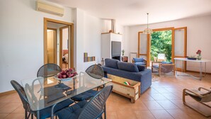 Uma sala de estar moderna com uma mesa de jantar de vidro, sofás azuis e uma mesa de centro de madeira.