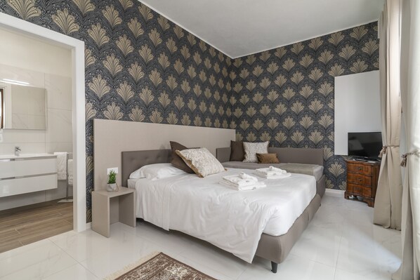 A modern bedroom with a large bed, a bedside table, a TV, and a bathroom with a sink and mirror. - Room 1 - Grifoni Boutique Hotel (Venice)
