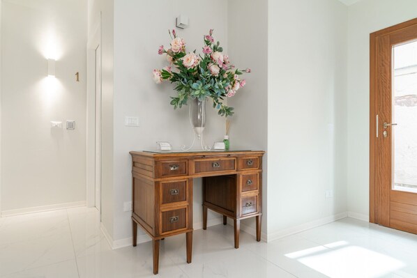 A wooden desk with drawers, a vase of flowers, and a door in a bright hallway. - Room 1 - Grifoni Boutique Hotel (Venice)