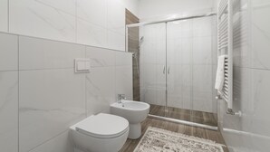 Un baño moderno con inodoro, bidé y ducha con mampara de vidrio.