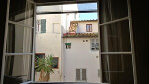 A view through an open window with a plant, a building with shutters, and a tiled roof. - Cozy and modern studio apartment by Mmega (Florence)